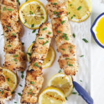 Grilled Chicken Spiedini skewers on a white plate with lemons and blue tongs