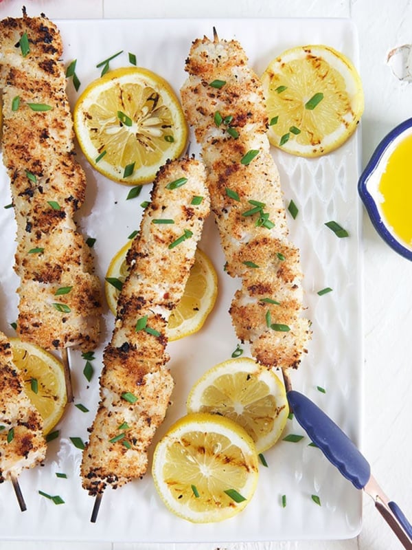 Grilled Chicken Spiedini skewers on a white plate with lemons and blue tongs