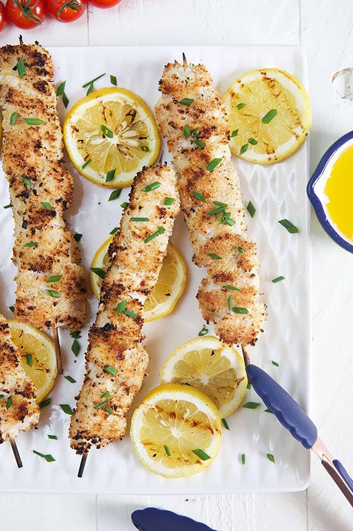 Grilled Chicken Spiedini skewers on a white plate with lemons and blue tongs