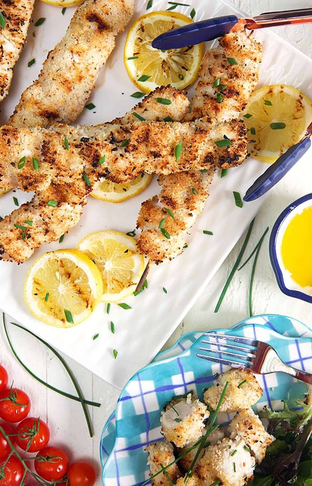 Chicken spiedini skewers on a white plate with lemon slices and a pile of grape tomatoes.