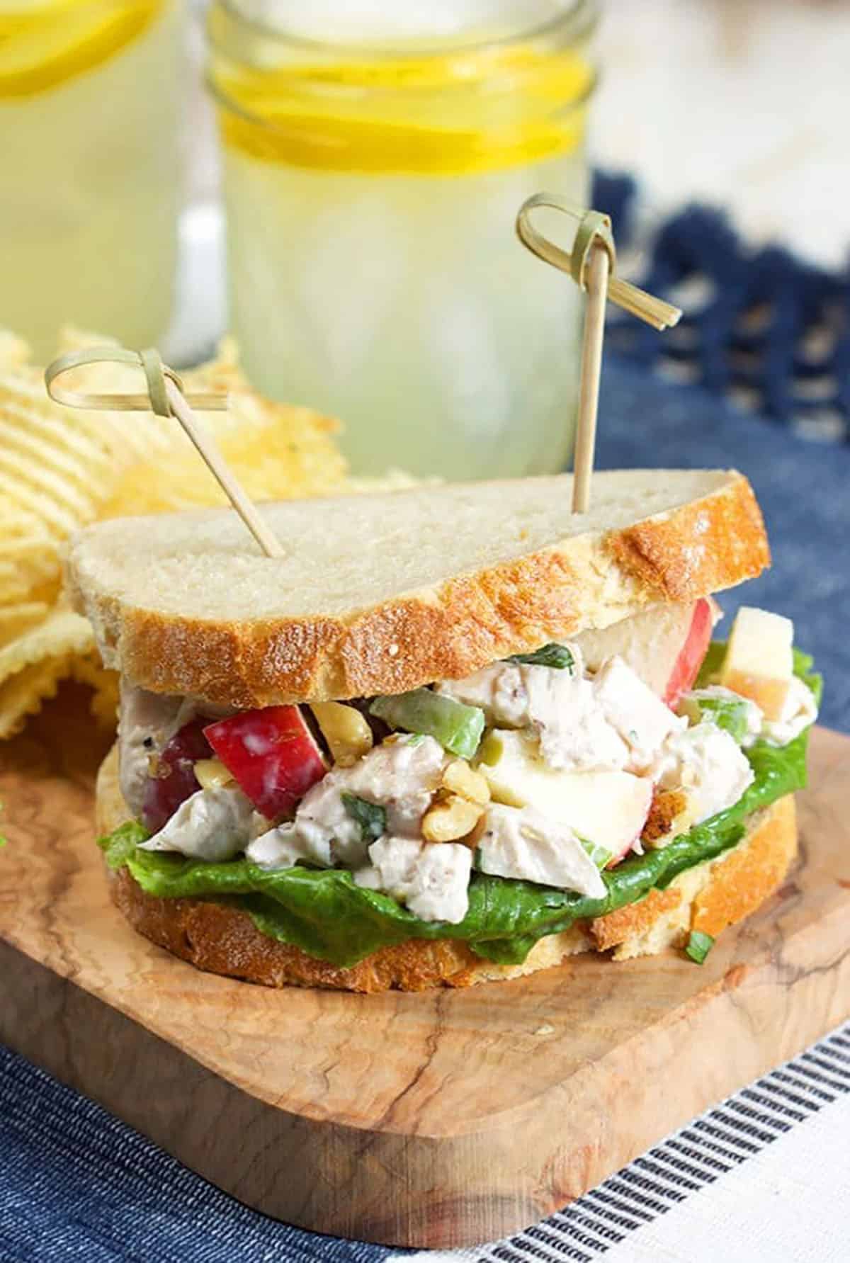 Chicken Waldorf Salad sandwich on a wooden board with potato chips.