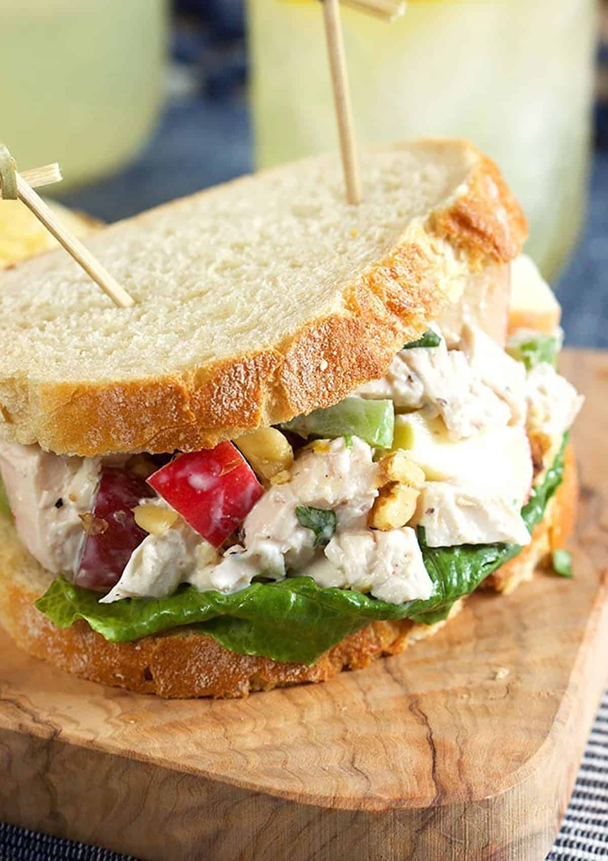 Chicken Waldorf Salad sandwich on an olive wood board with toothpicks.