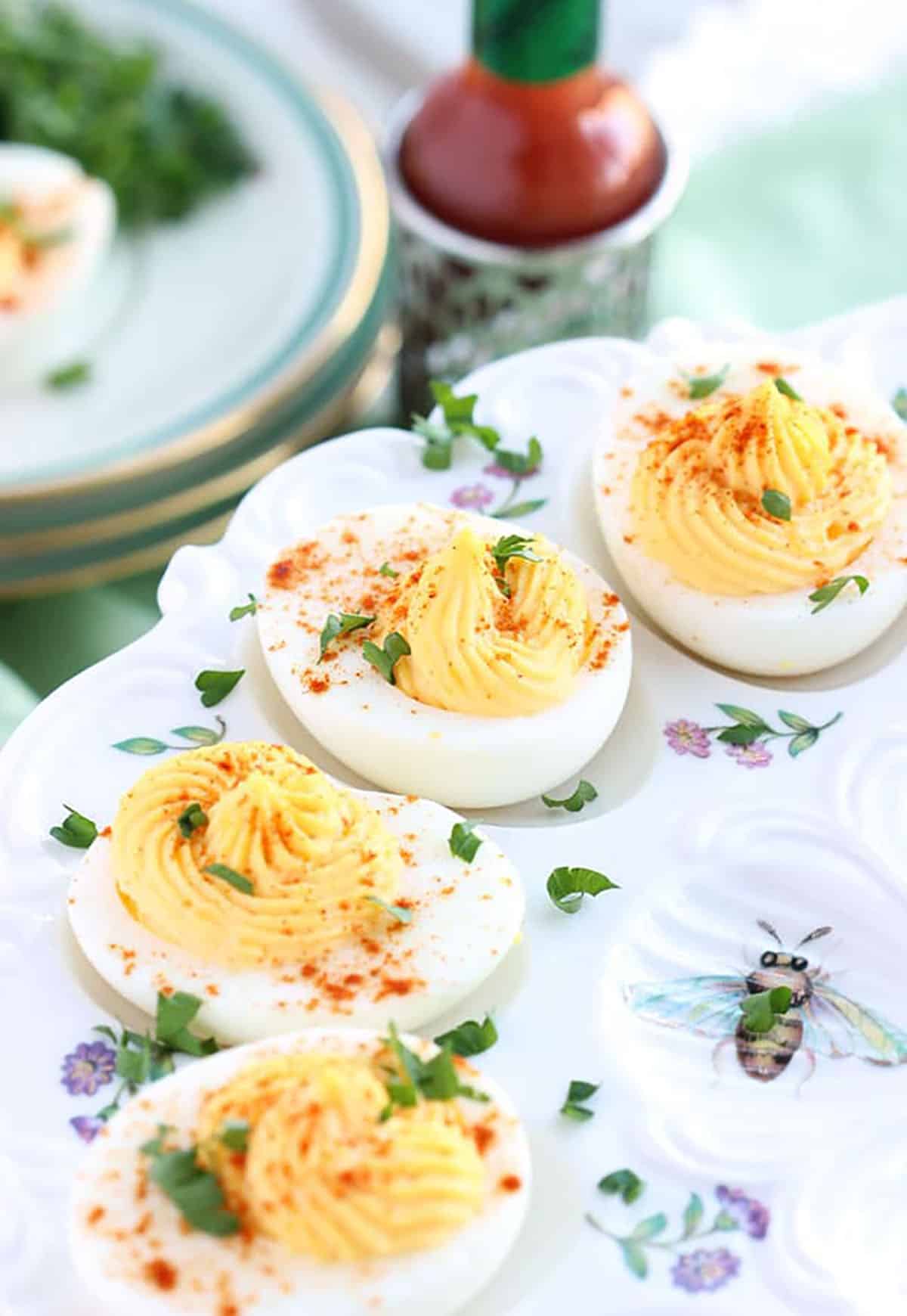 Deviled Eggs on a floral plate with a bottle of hot sauce in the background