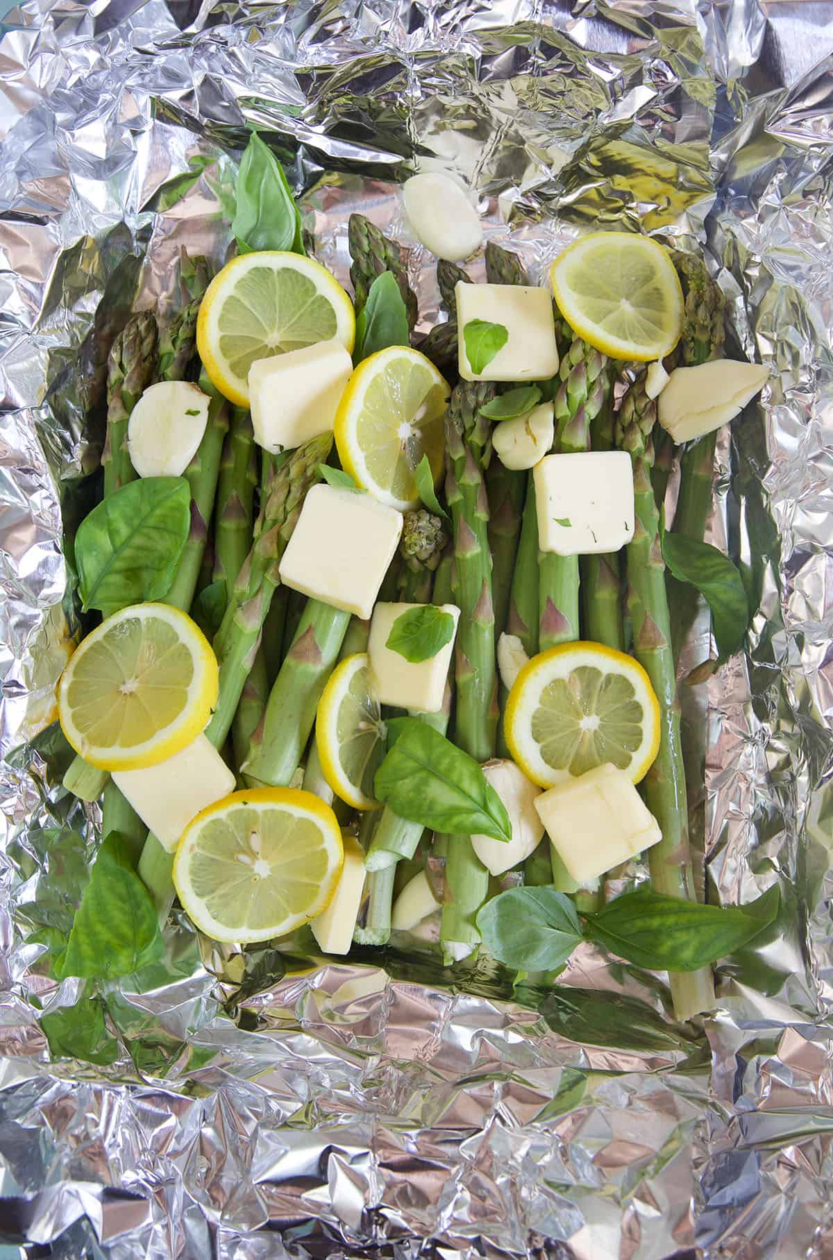 Asparagus is covered in squares of butter, lemon slices, and basil. 