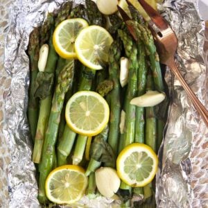 Asparagus is cooked and wrapped in foil, topped with lemon slices.