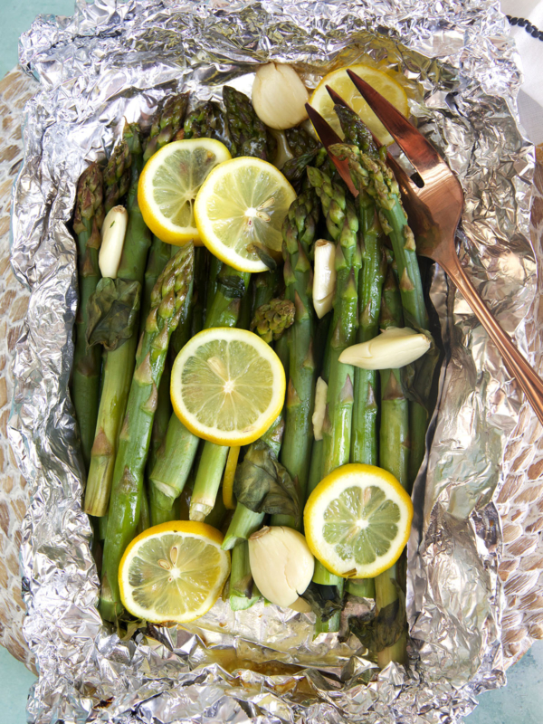 Asparagus is cooked and wrapped in foil, topped with lemon slices.