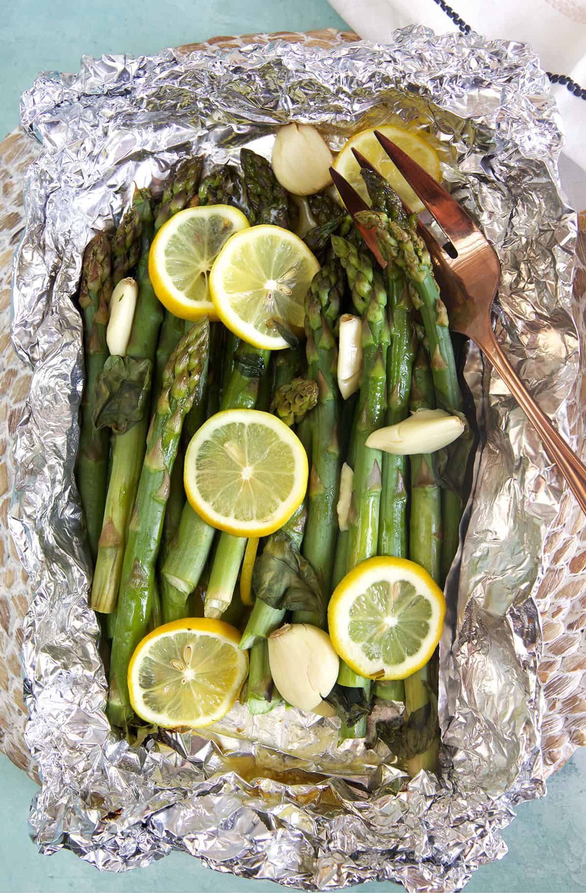 Asparagus is cooked and wrapped in foil, topped with lemon slices. 