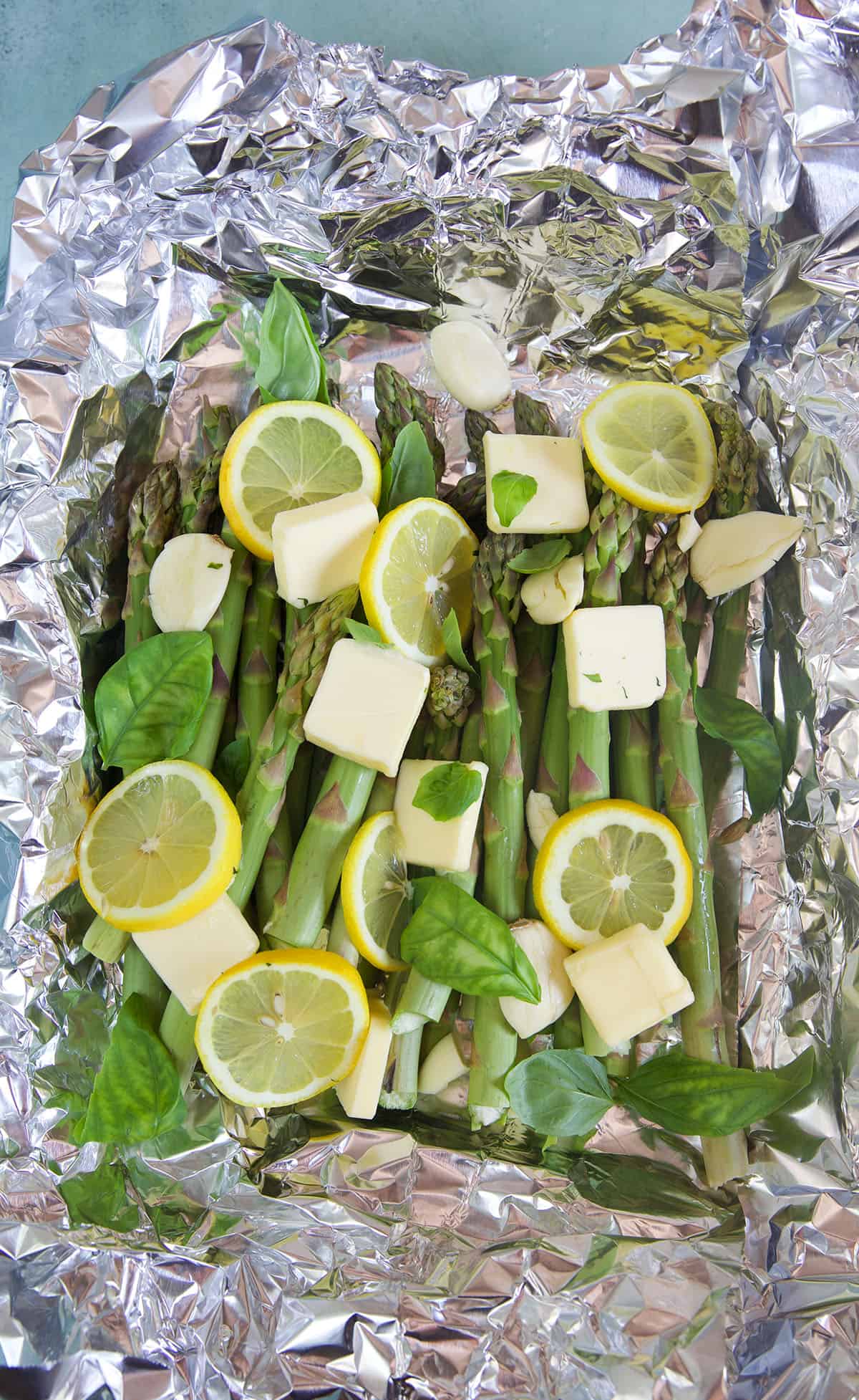 Asparagus with fresh toppings is wrapped in foil and ready to be grilled. 