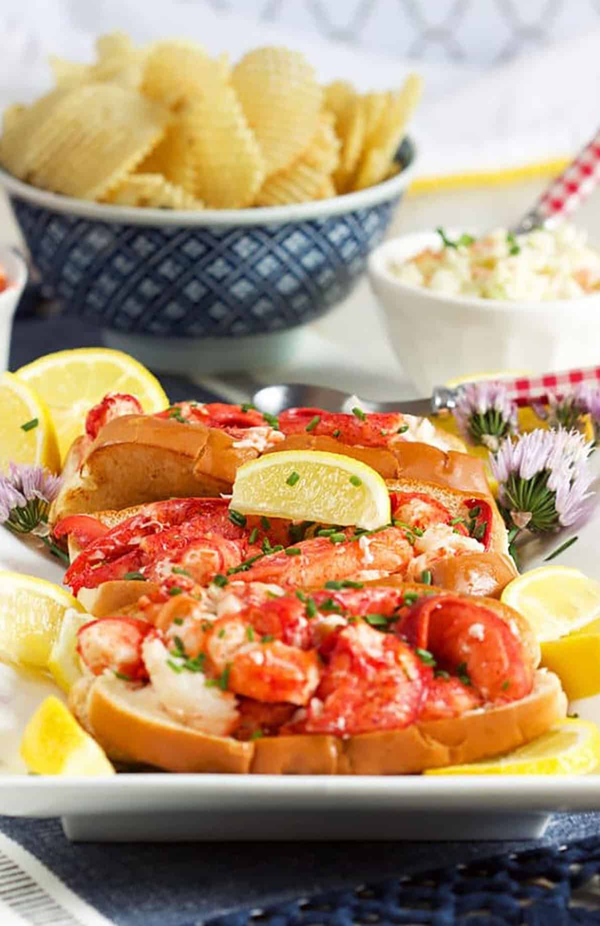 Lobster Rolls on a platter with a bowl of chips in the background.