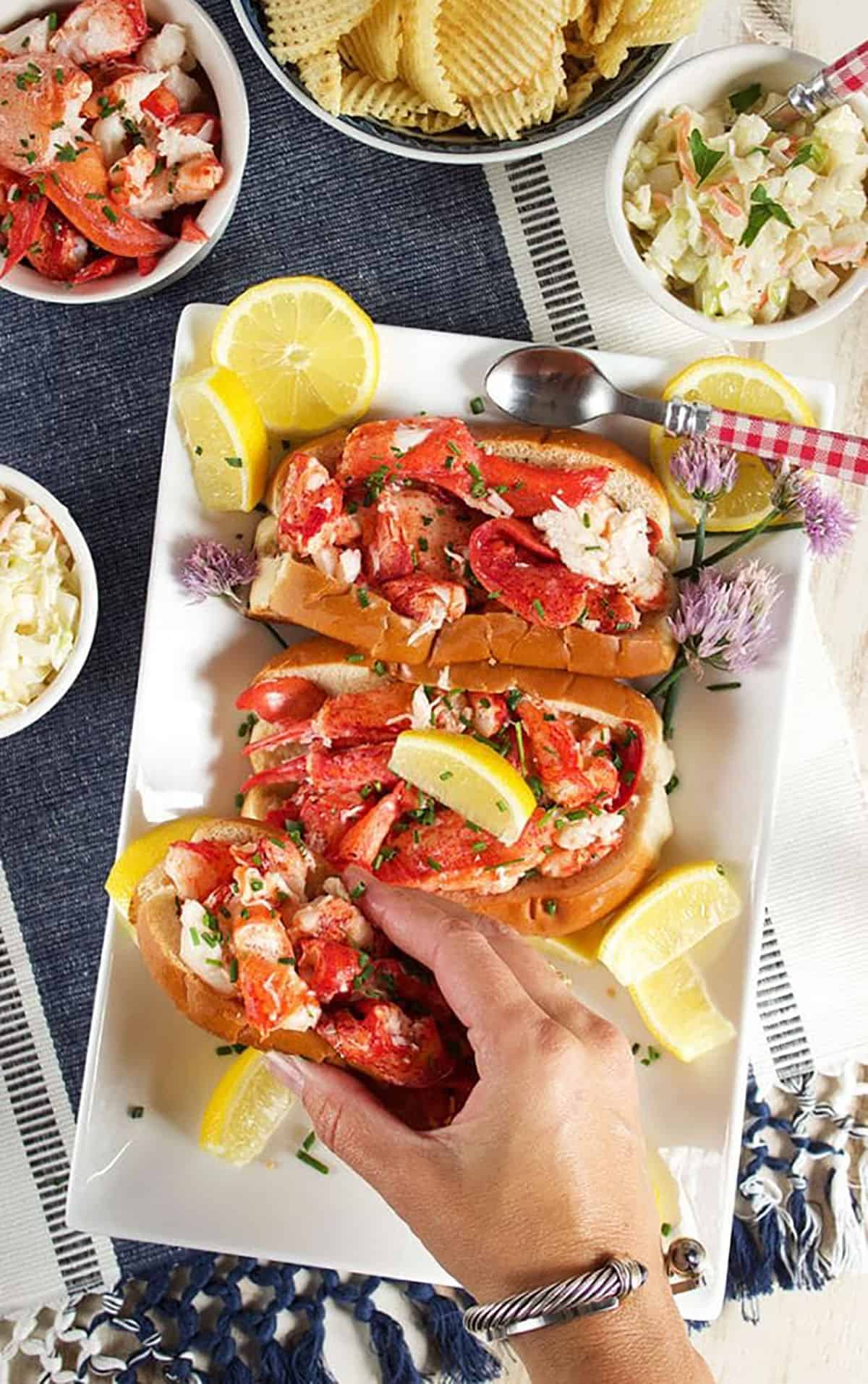 Lobster rolls on a platter with a hand taking one off the plate.