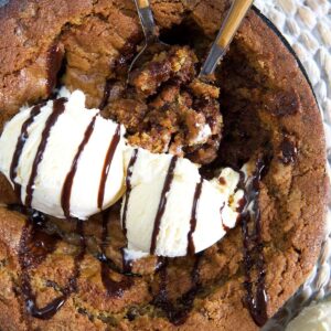 Two dollops of vanilla ice cream are placed on top of a warm pizookie.