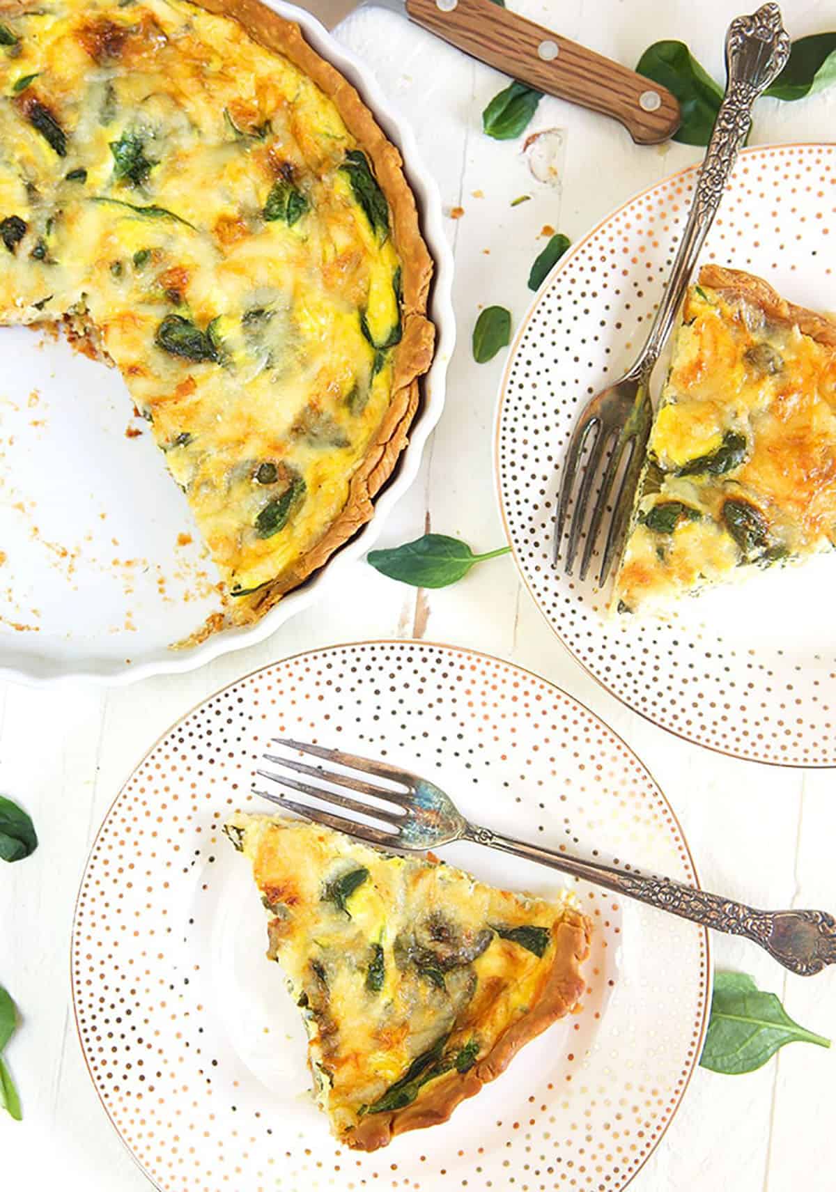 Overhead shot of two slices of Quiche Florentine on a white plate with a tarnished silver fork.