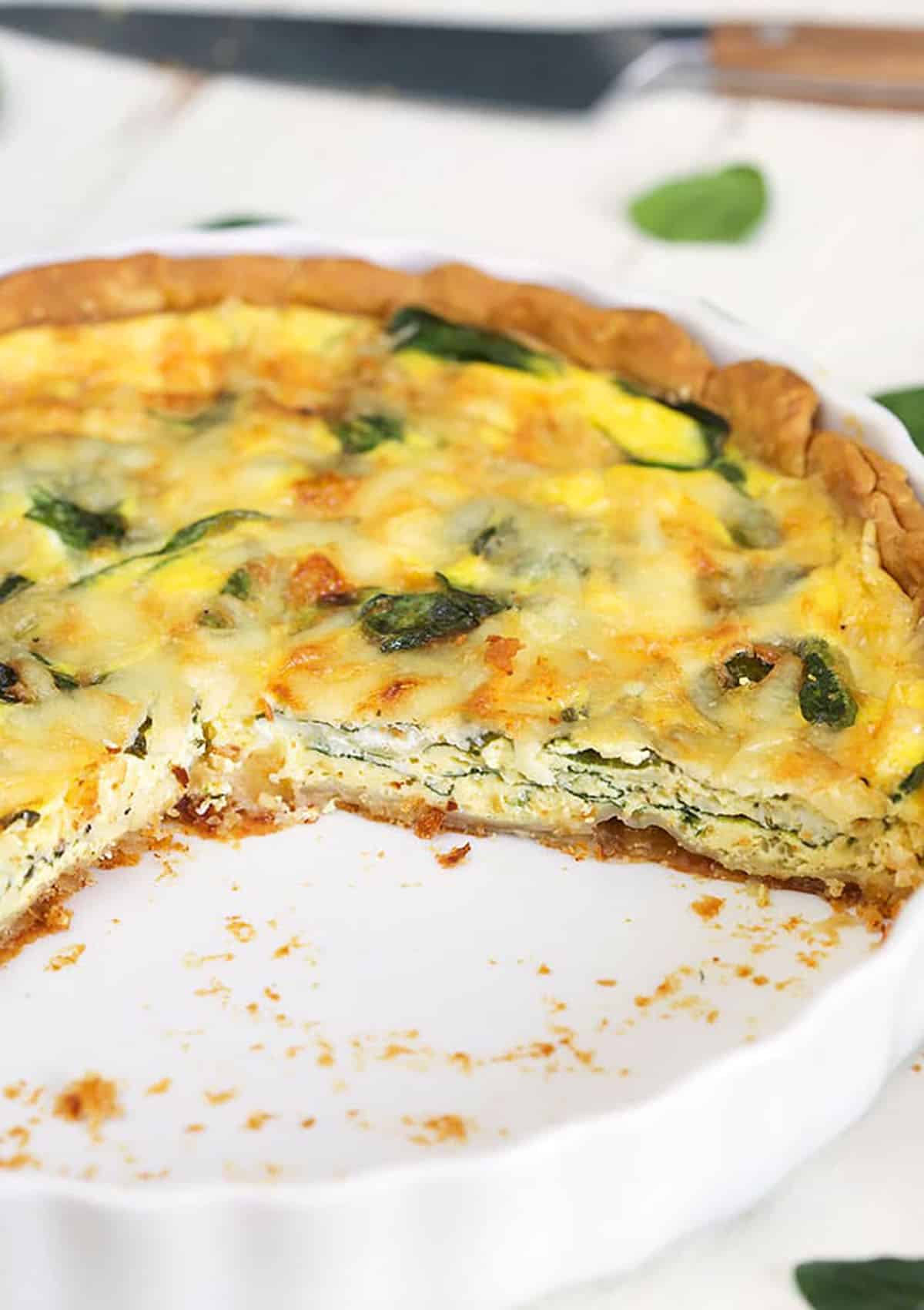 Quiche Florentine in a white pie plate with a slice cut out of it.