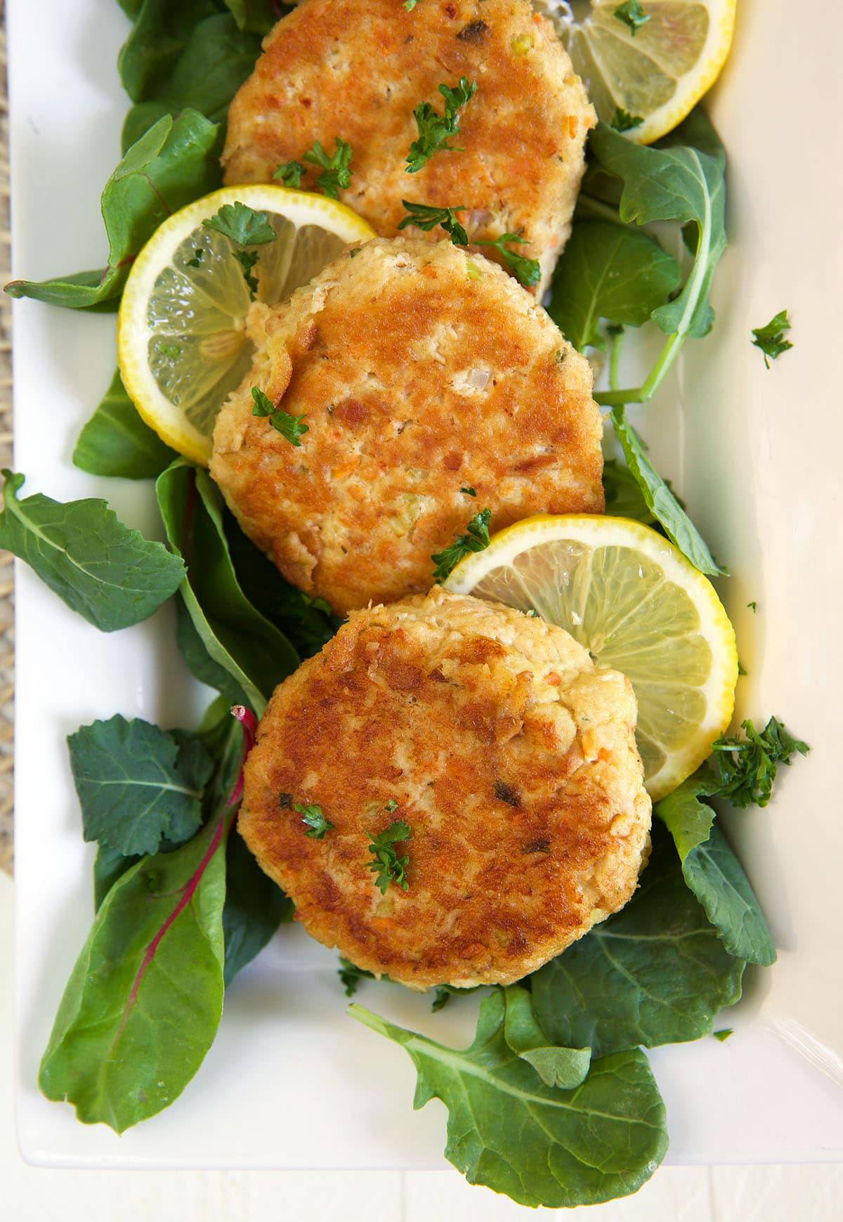 Tuna patties are placed on a plate next to lemon slices and leafy greens.