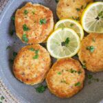 Tuna patties are arranged in a large skillet with lemon slices.