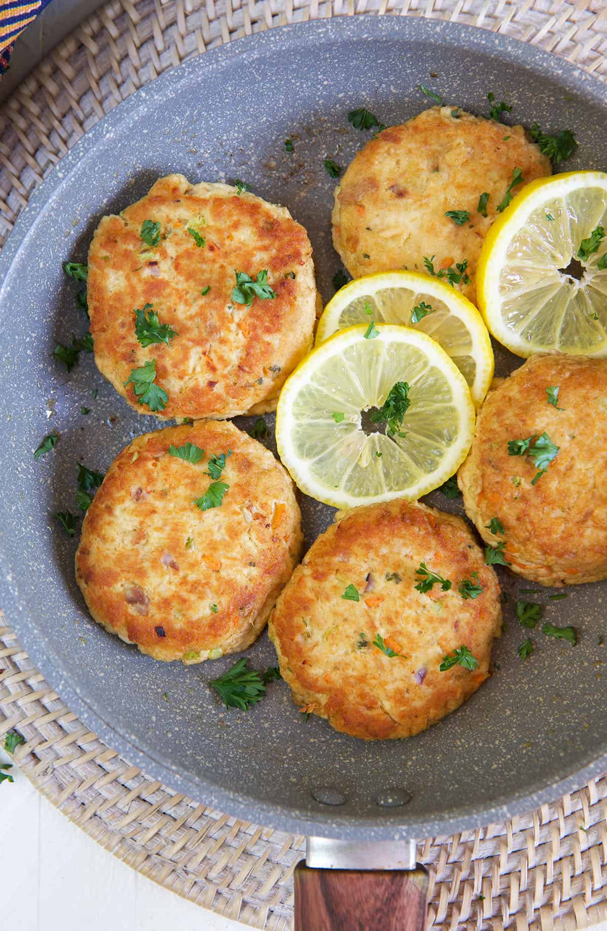 Tuna patties are arranged in a large skillet with lemon slices. 