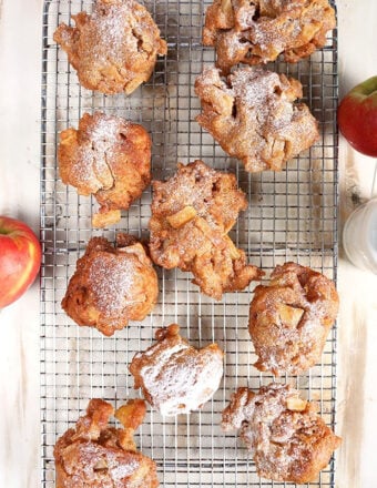 Apple fritters on a cooling rack on a rustic white background with apples