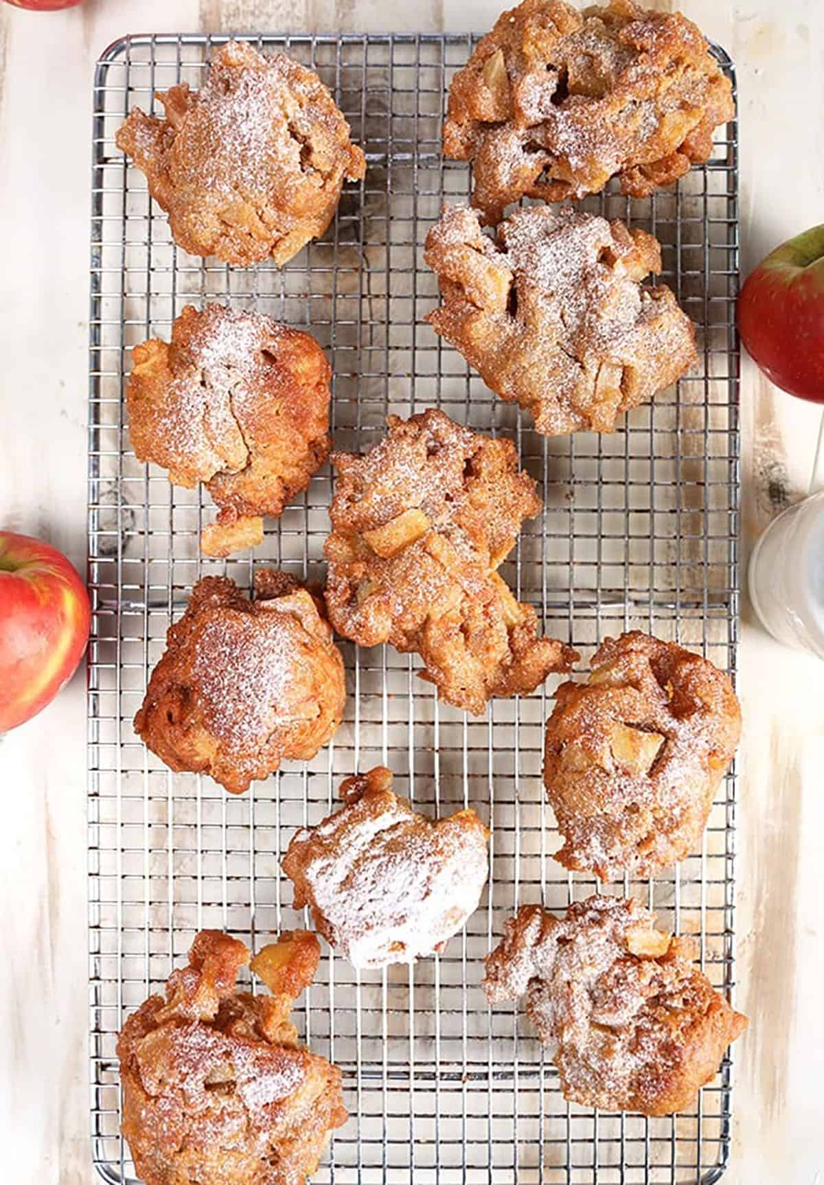 Apple fritters on a cooling rack on a rustic white background with apples