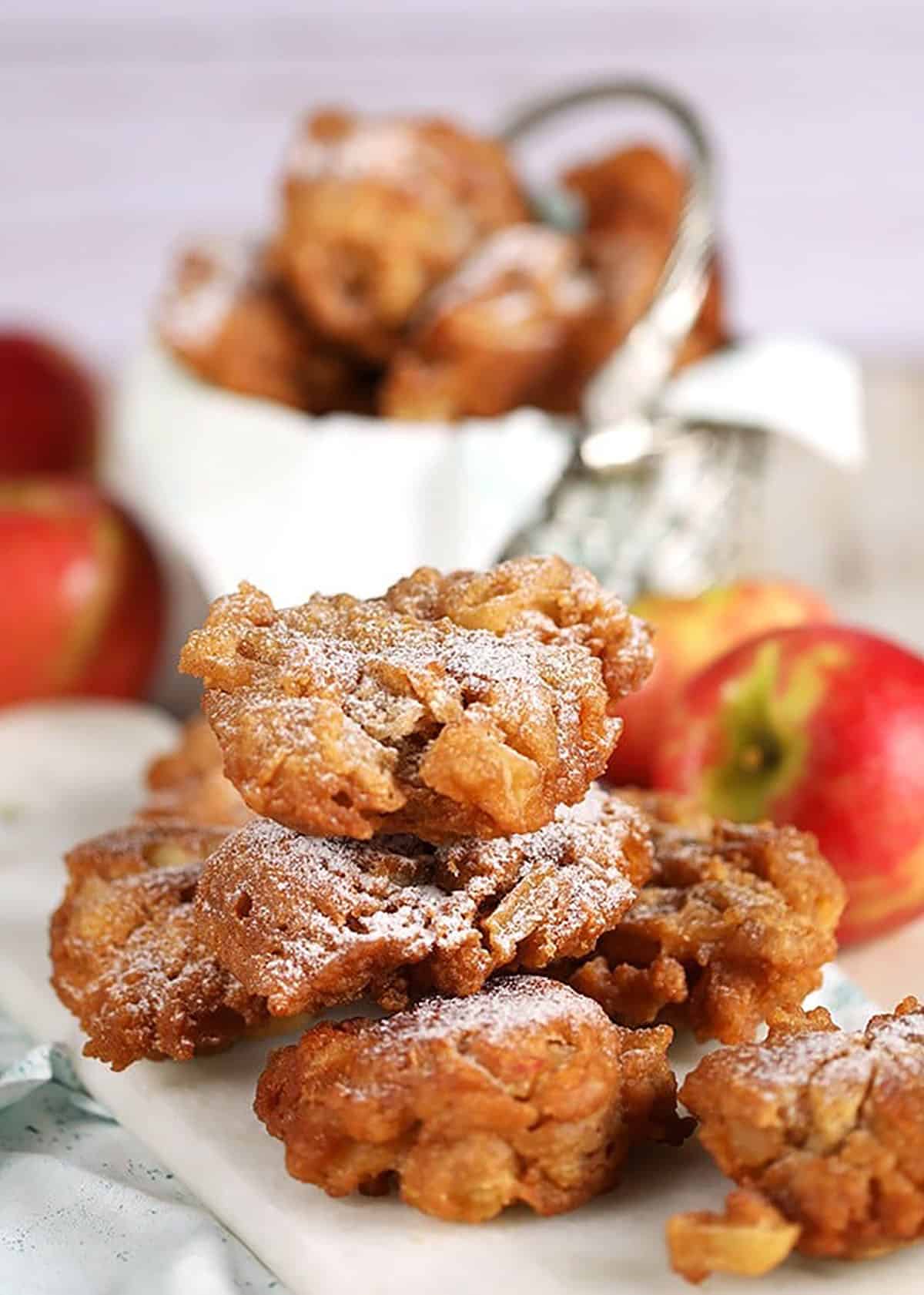 Apple fritters piled in a metal basket with a white napkin.