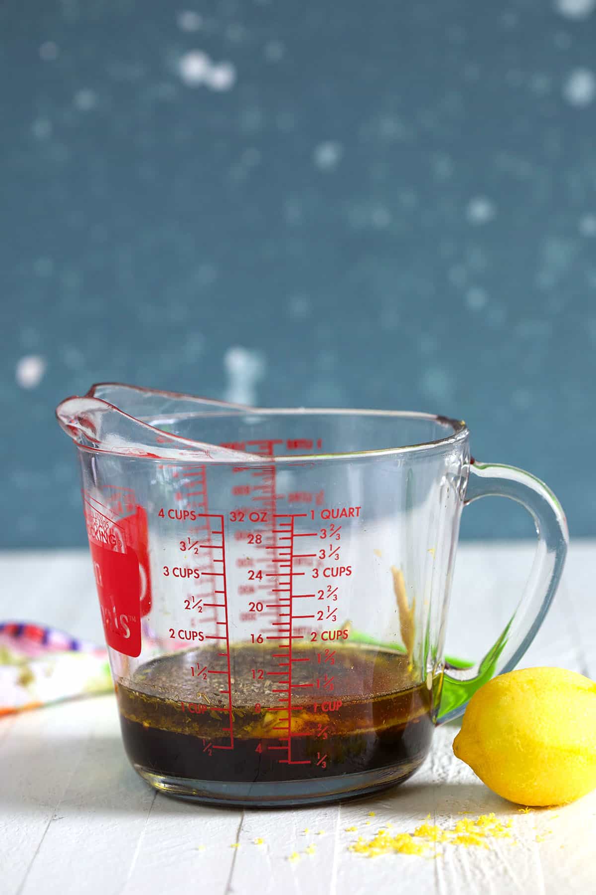 A measuring cup is placed next to a lemon on a white surface. 