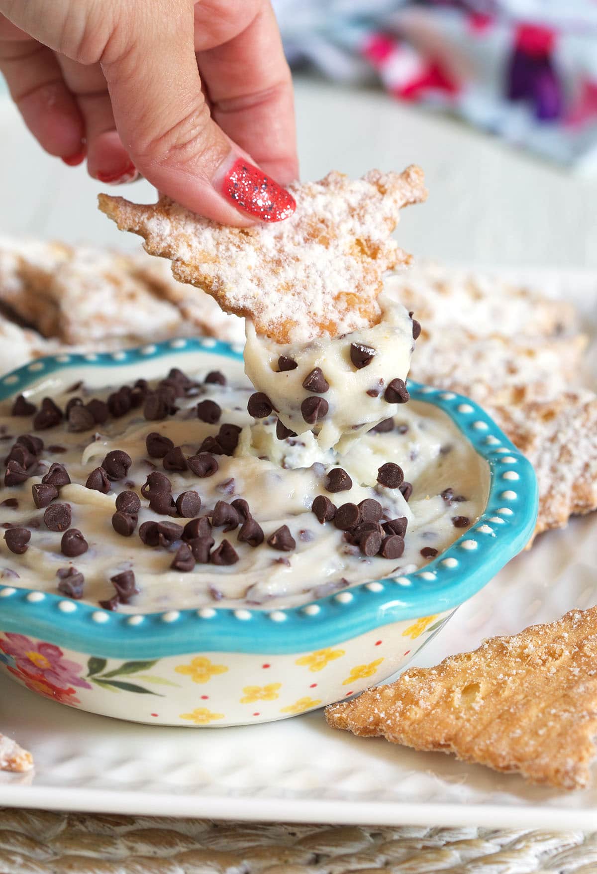 A hand is dipping a cannoli shell into the dip.