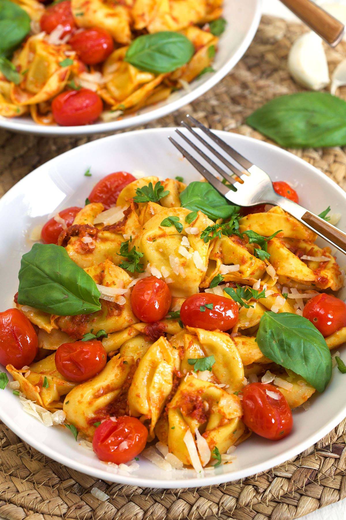 A tortellini bowl is topped with basil, tomatoes, parmesan and parsley. 