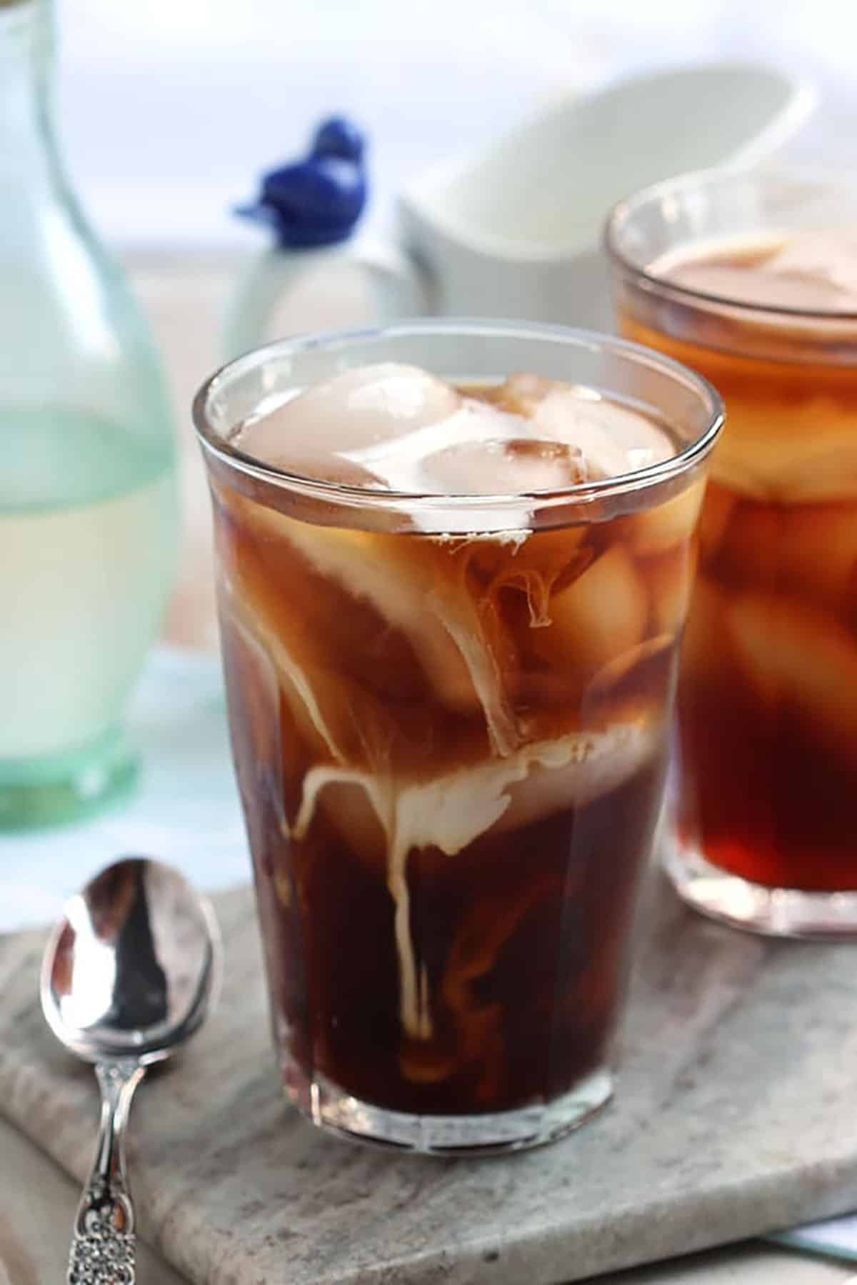 Cold Brew Coffee in a glass with ice and a spoon to the left of the glass on a marble board.