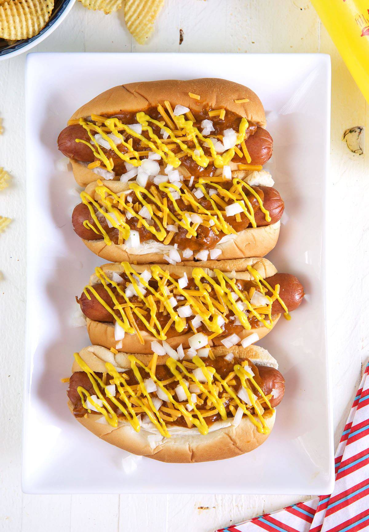 Four hot dogs are placed on a white rectangular plate. 