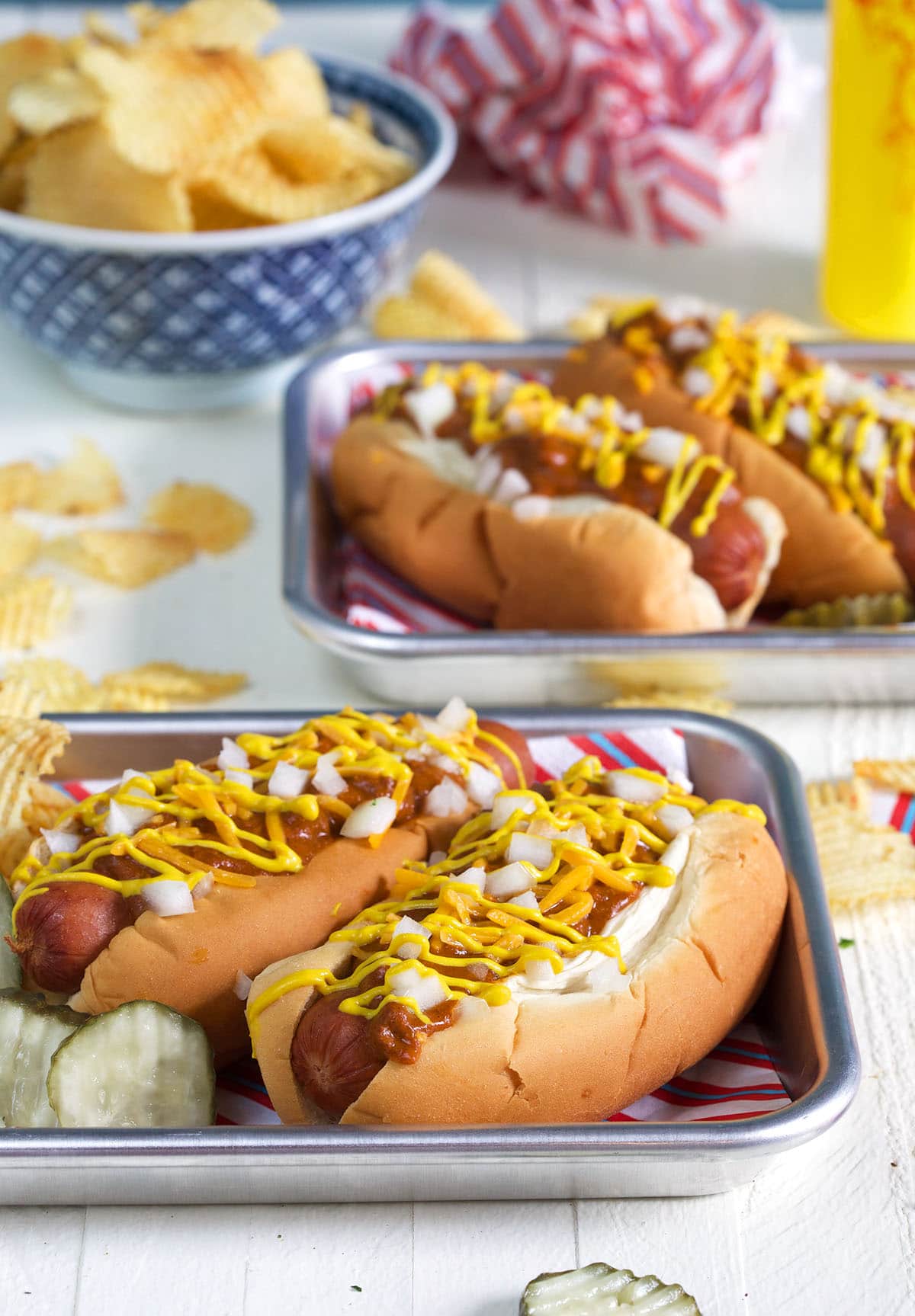 Four hot dogs are placed on two separate metal serving trays. 