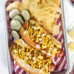 Pickles and fries are placed next to two Coney Island hot dogs on a metal tray lined with patriotic paper.