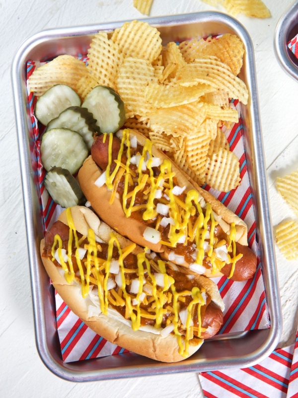 Pickles and fries are placed next to two Coney Island hot dogs on a metal tray lined with patriotic paper.