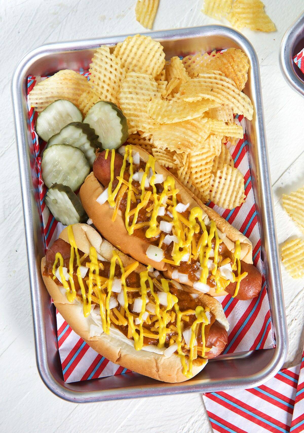 Pickles and fries are placed next to two Coney Island hot dogs on a metal tray lined with patriotic paper. 