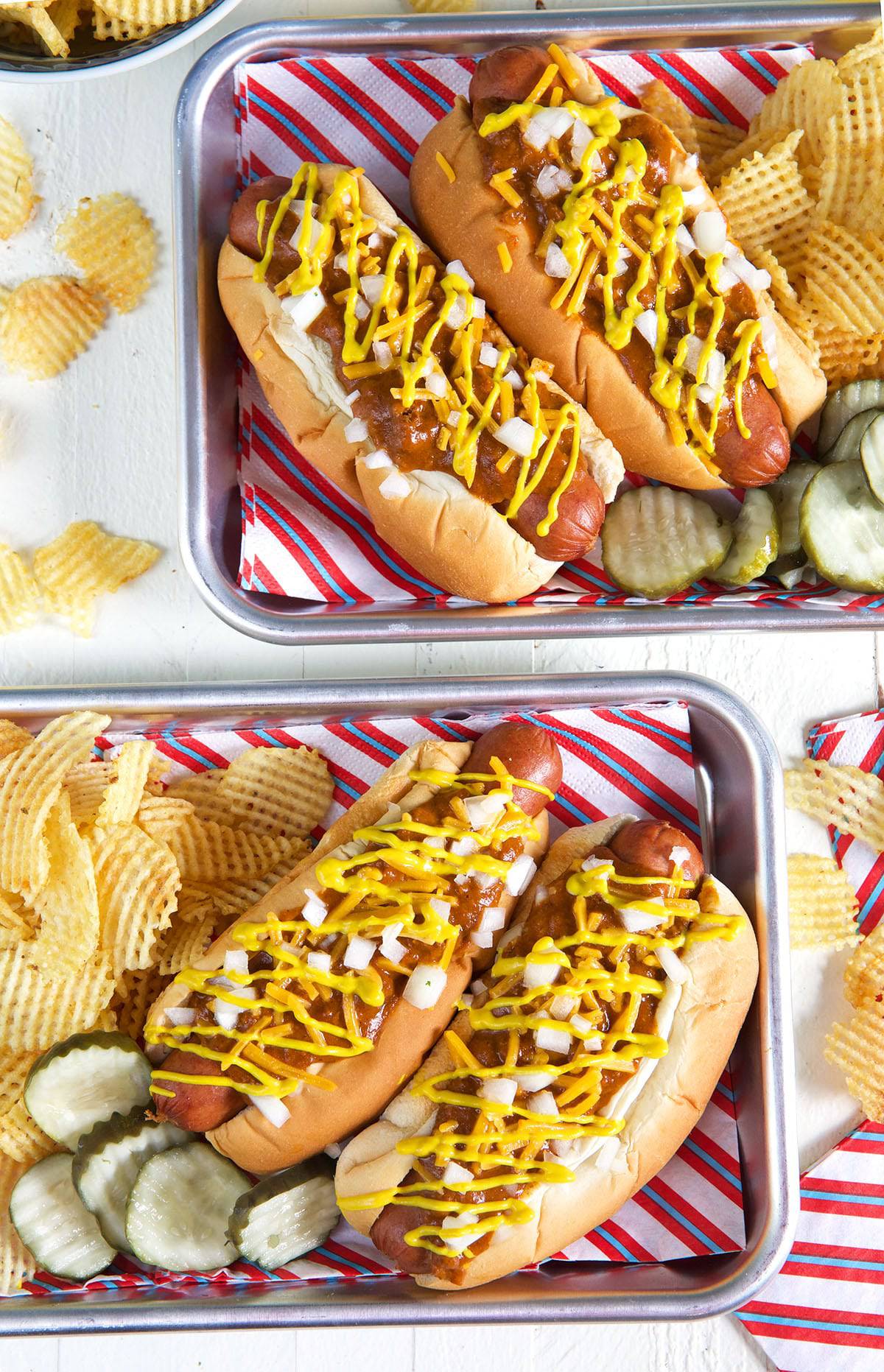 Four hot dogs are ready to be eaten on metal trays. 