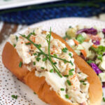 A crab salad roll is garnished with chives on a white plate.