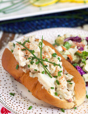 A crab salad roll is garnished with chives on a white plate.
