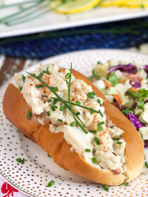 A crab salad roll is garnished with chives on a white plate.