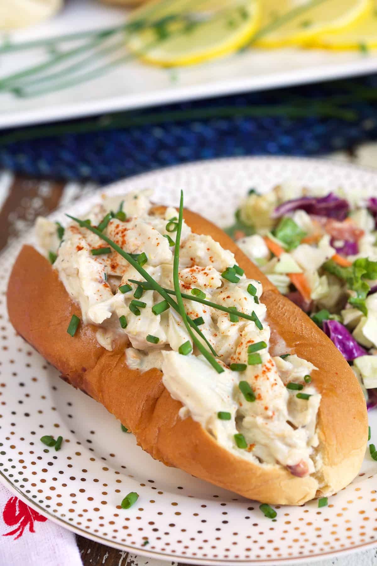 A crab salad roll is garnished with chives on a white plate. 