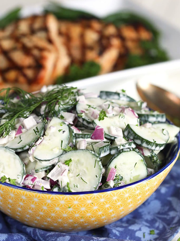 Creamy Cucumber Salad in a yellow bowl on a blue napkin.