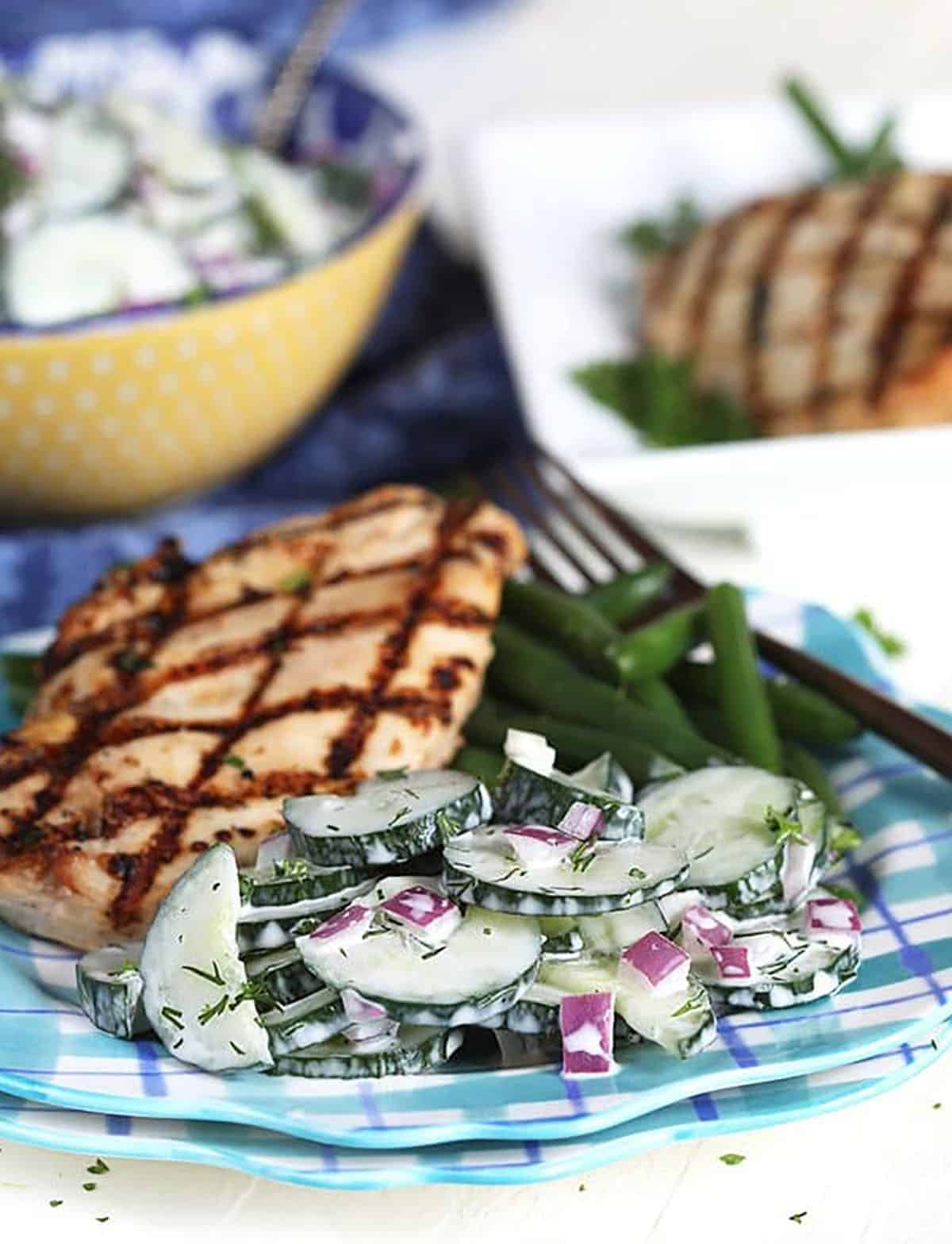 Creamy cucumber salad on a plate with grilled chicken breast.