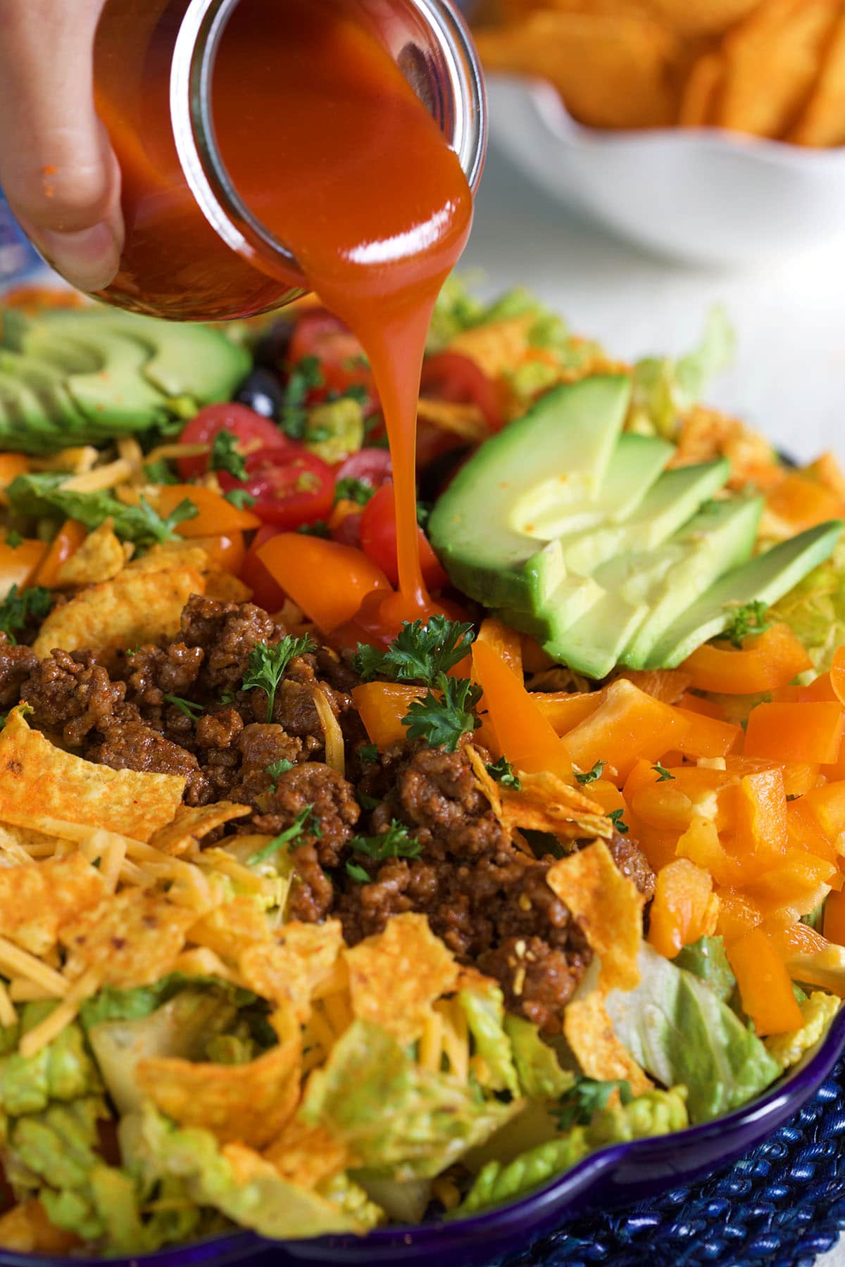Salad dressing is being poured over the taco salad. 