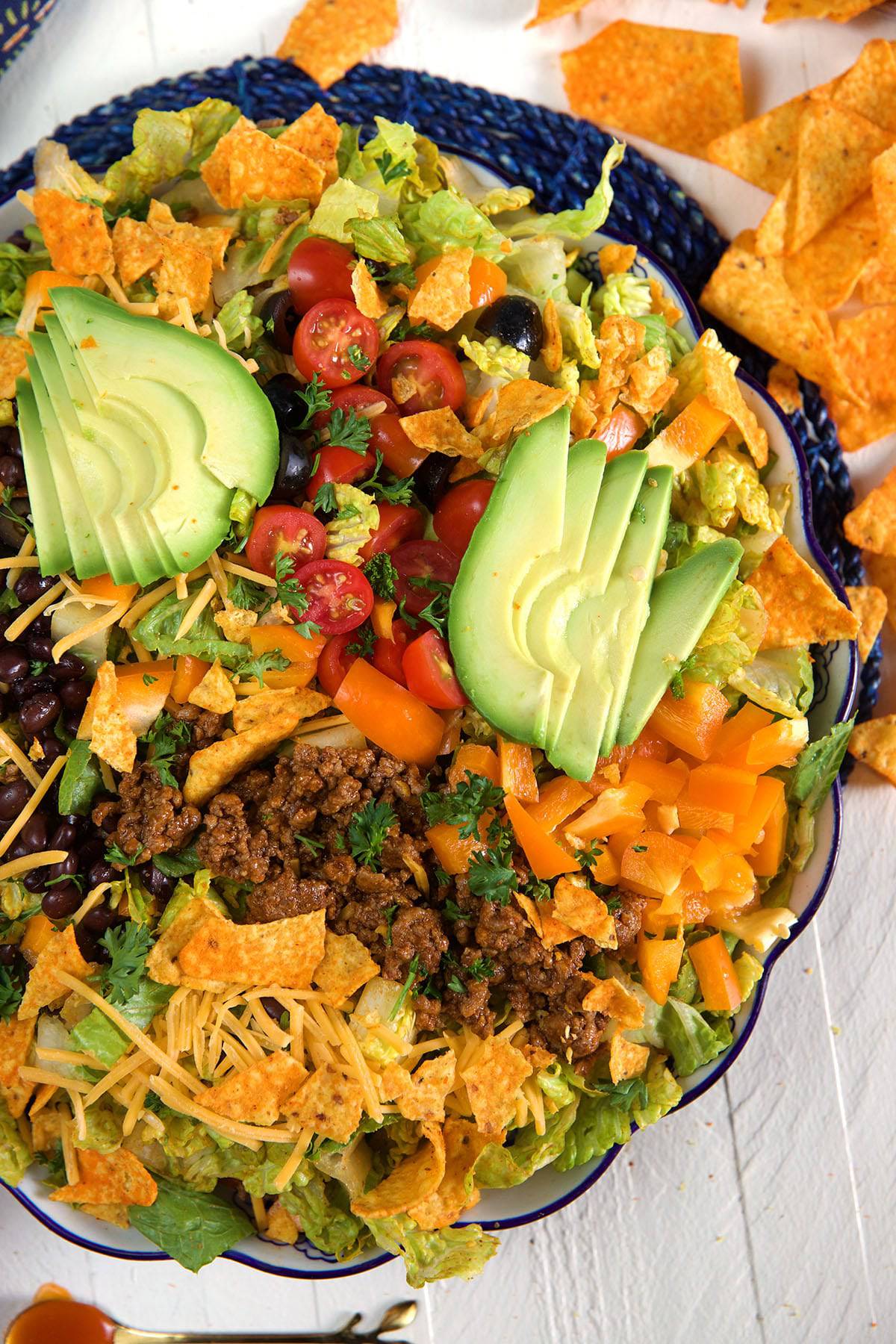 Doritos are spread out on a white surface surrounding a big bowl of taco salad. 