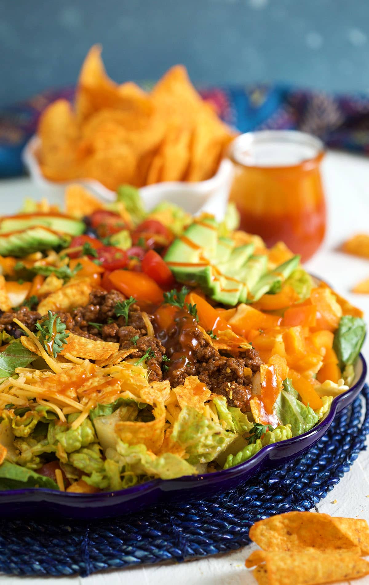 Taco salad is served on a large blue plate and is ready to eat. 