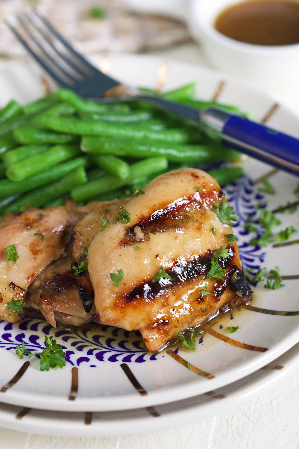 Grilled and glazed chicken thighs are on a plate with green beans. 