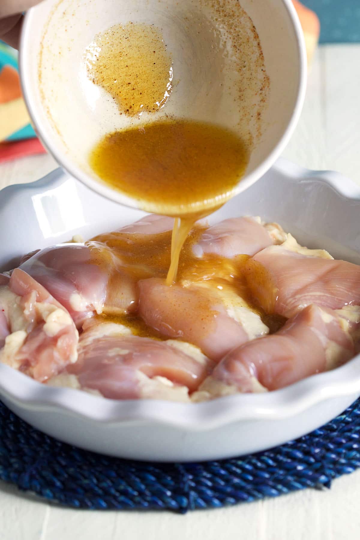 Marinade is being poured over uncooked chicken. 