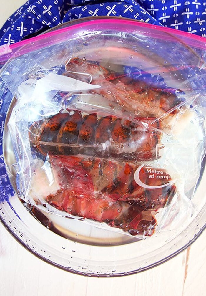Frozen Lobster Tails in a plastic bag in a bowl of water.