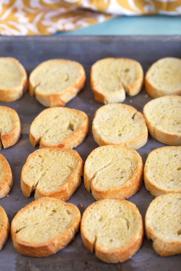 Slices of toasted crostini are on a baking sheet. 
