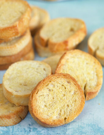 Little golden pieces of crostini are placed on a blue surface.