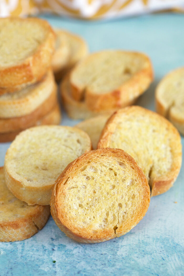 Little golden pieces of crostini are placed on a blue surface. 