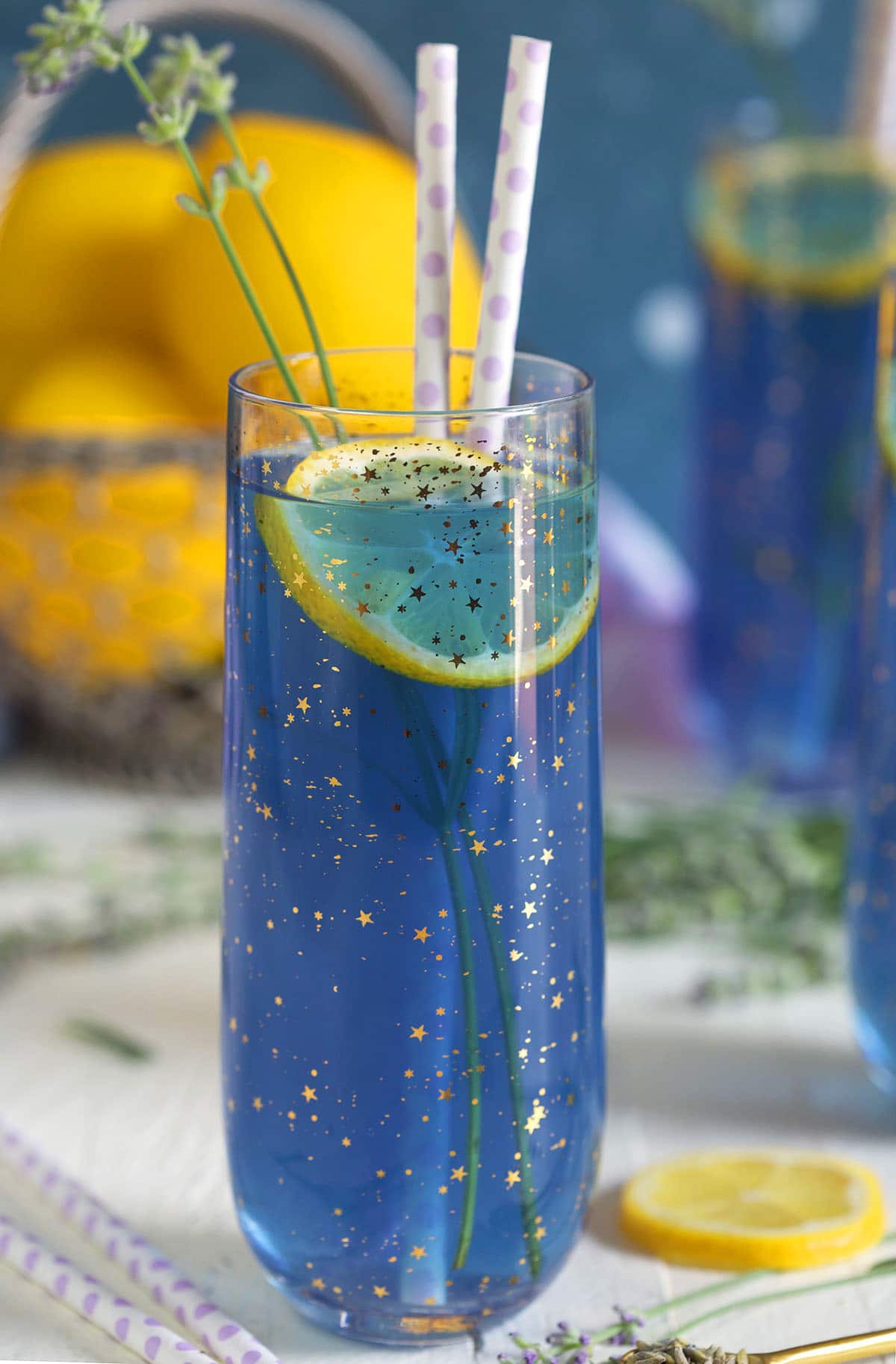A glass filled with lavender lemonade is on a white surface. 