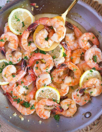 Overhead shot of lemon garlic shrimp in a skillet with a gold serving spoon and lemon slices.